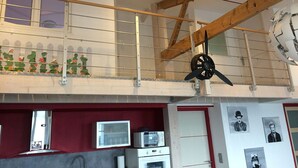 Ein Zimmer mit Holzboden, Deckenventilator, Fenster, Fernseher und Kühlschrank.