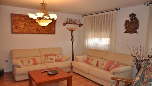 Una sala de estar con dos sofás beige, una mesa de centro de madera, una araña, una lámpara de pie y una silla decorativa.