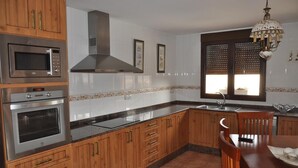 Una cocina con armarios de madera, electrodomésticos de acero inoxidable, salpicadero de azulejos y un comedor con mesa y sillas.