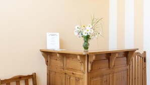 A reception desk with a vase of flowers, a wooden chair, and a wall-mounted lamp.