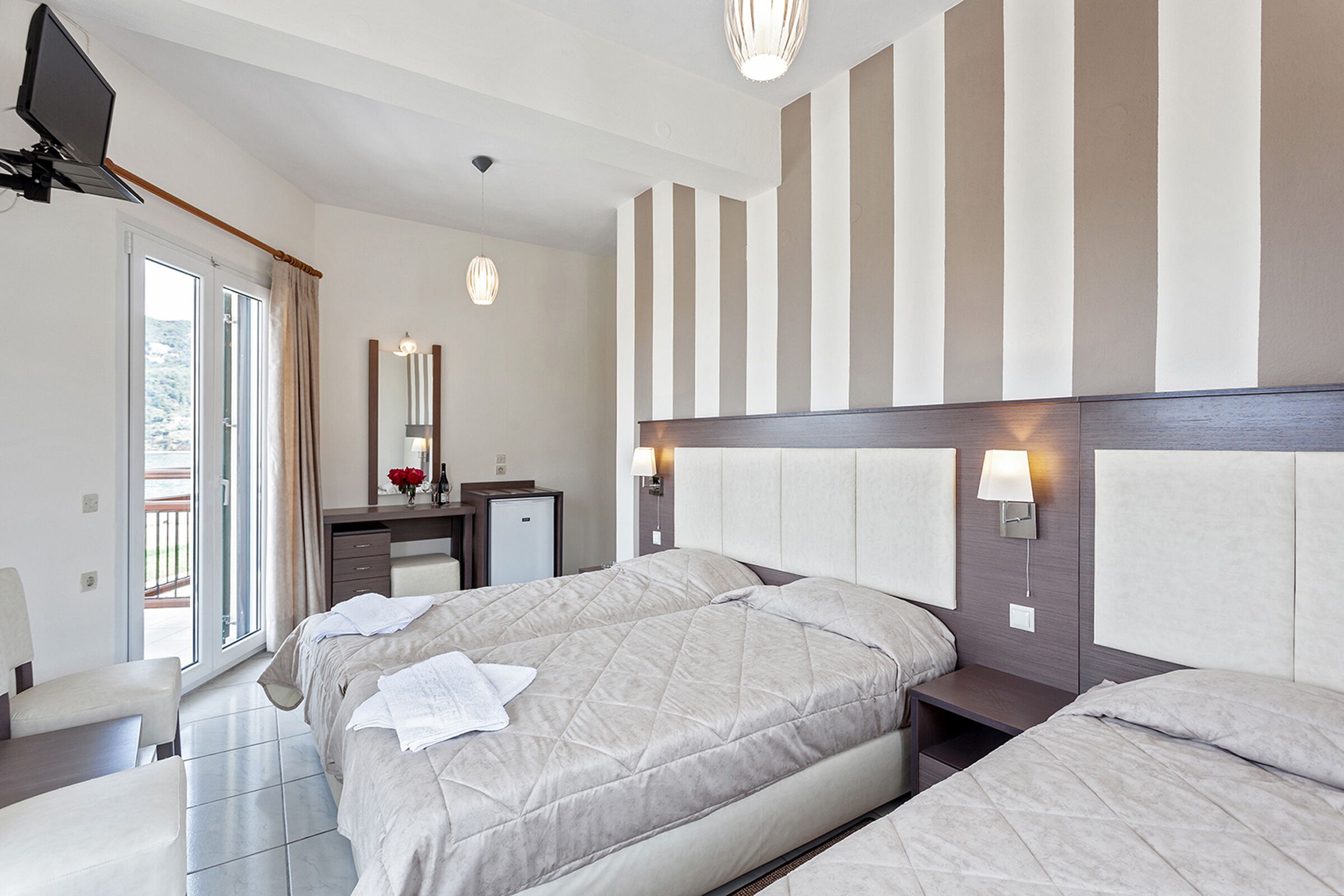 A hotel room with a bed, bedside tables, a desk, a chair, a TV, and a window with curtains.