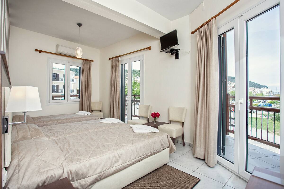 A hotel room with a large bed, two chairs, a small table with a vase of flowers, and a TV mounted on the wall.