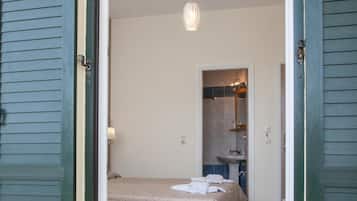 An open door leading to a bedroom with a bed, a bedside table, and a hanging light fixture.