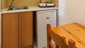 A compact kitchen with wooden cabinets, a sink, a small refrigerator, and a wooden dining table with chairs.
