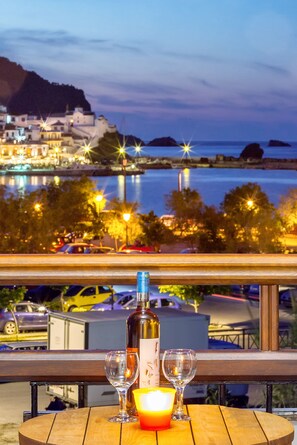 Mesa con una botella y dos vasos, con vista a un muelle con edificios y barcos.