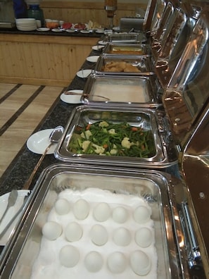 A buffet with various food options including a container of white spherical items, a tray of green vegetables, and a container of brownish food items. - Hotel Grenville (Gurugram)