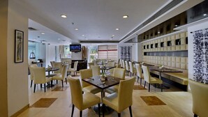 A modern restaurant with multiple dining tables and chairs, a television mounted on the wall, and a patterned wall decoration. - Hotel Grenville (Gurugram)