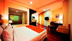 A hotel room with a large bed, a desk, a chair, a television, and a window with curtains. - Hotel Grenville (Gurugram)