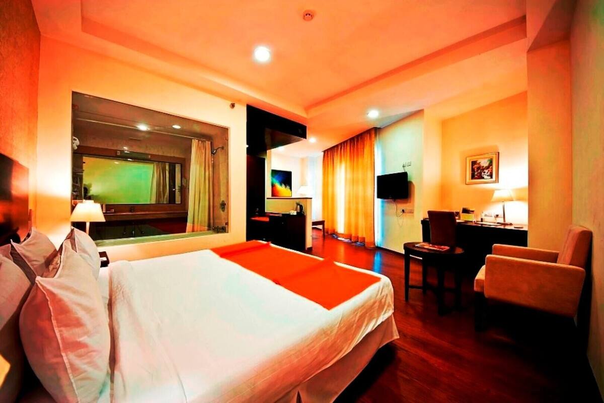 A hotel room with a large bed, a desk, a chair, a television, and a window with curtains.