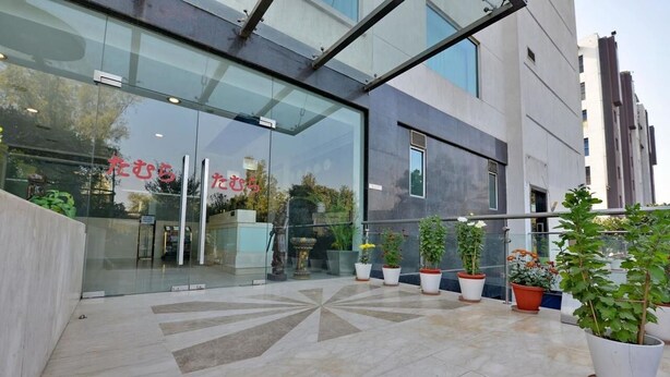 A modern building entrance with glass doors, potted plants, and a geometric tile pattern on the floor. - Hotel Grenville (Gurugram)