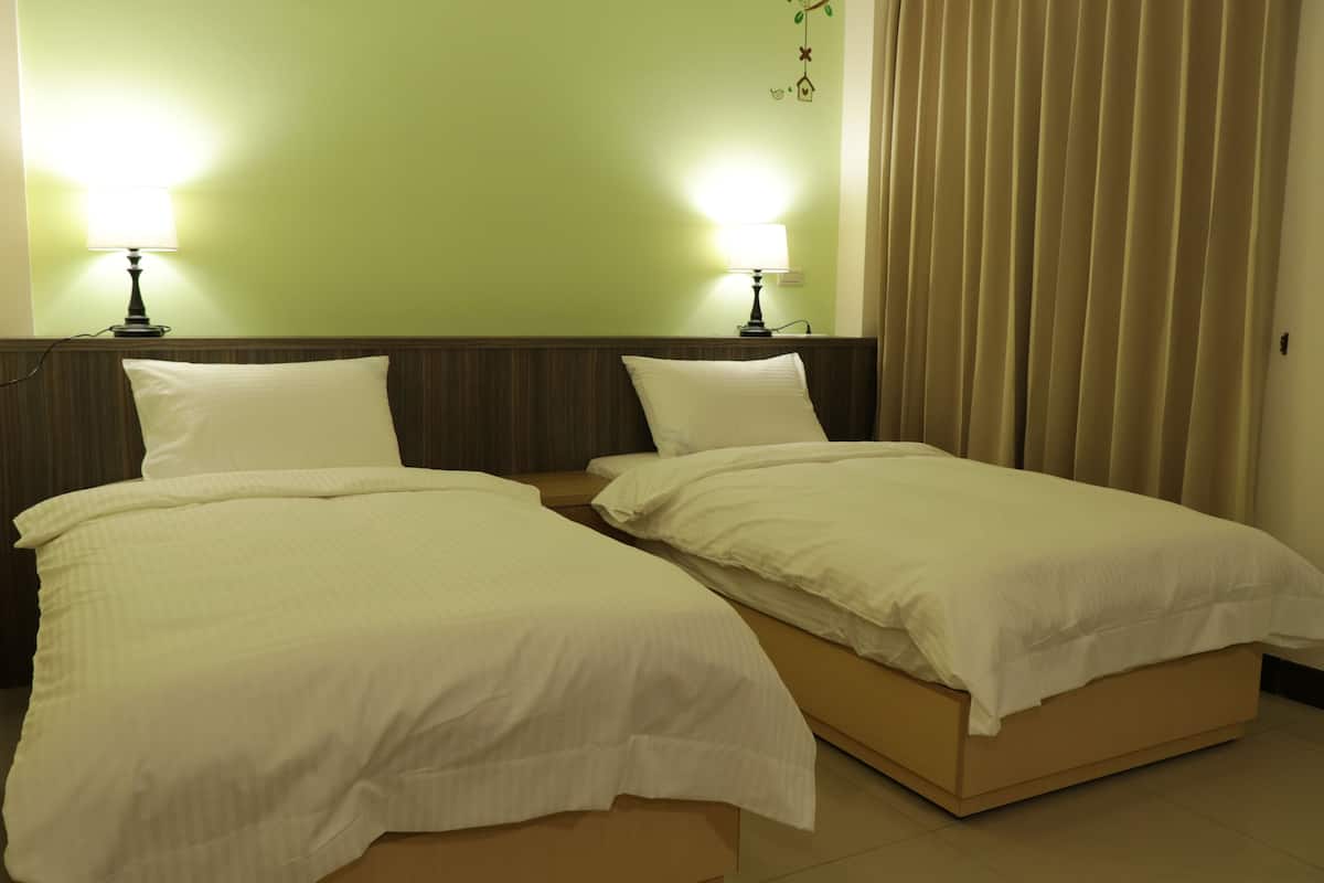 Habitación de hotel con dos camas individuales, cada una con una almohada y una mesita de noche. Hay dos lámparas de pared a cada lado de las camas.