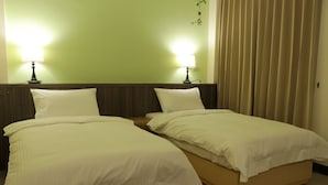 Une chambre d’hôtel avec deux lits simples, chacun équipé d’un oreiller et d’une table de chevet. Deux lampes murales sont fixées de part et d’autre des lits.