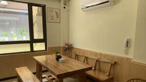 Un coin repas en bois avec une table et des bancs, une fenêtre avec des stores, un appareil de climatisation et un téléphone fixé au mur.
