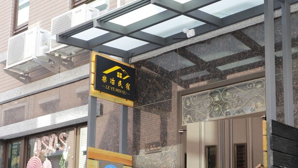 L’entrée d’un hôtel au design moderne, avec un auvent en verre, une grande plante en pot et une enseigne avec des caractères chinois.