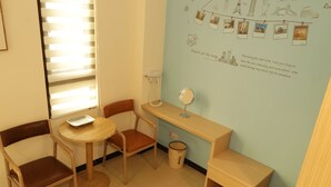 Une petite pièce bien éclairée, avec un bureau en bois, une chaise, une petite table et un mur décoré de photos et de textes sur le thème du voyage.