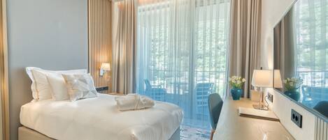 Habitación de hotel moderna con una cama grande, un escritorio con silla, televisión y vistas al exterior a través de amplios ventanales.