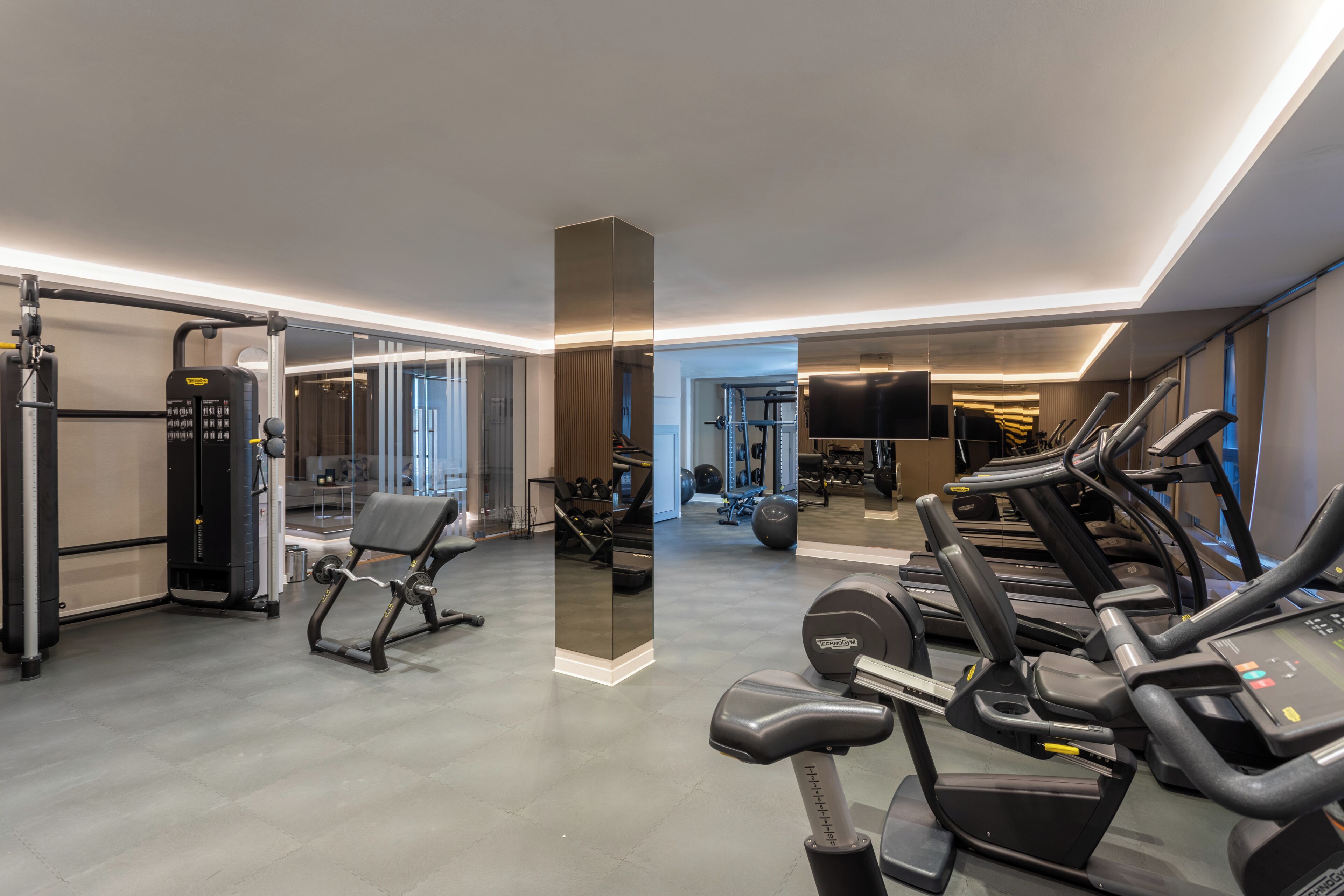 Un gimnasio moderno con cintas de correr, máquinas de pesas y un espejo grande.