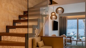 Un intérieur moderne avec un escalier en bois, des rampes de protection en verre et un coin salon offrant une vue sur la mer.