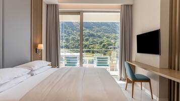 Habitación de hotel con una cama grande, un escritorio con silla, televisión y balcón con vistas a las montañas.