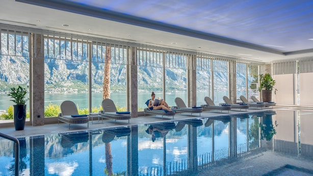 An indoor swimming pool with clear views of a mountainous landscape through large windows.