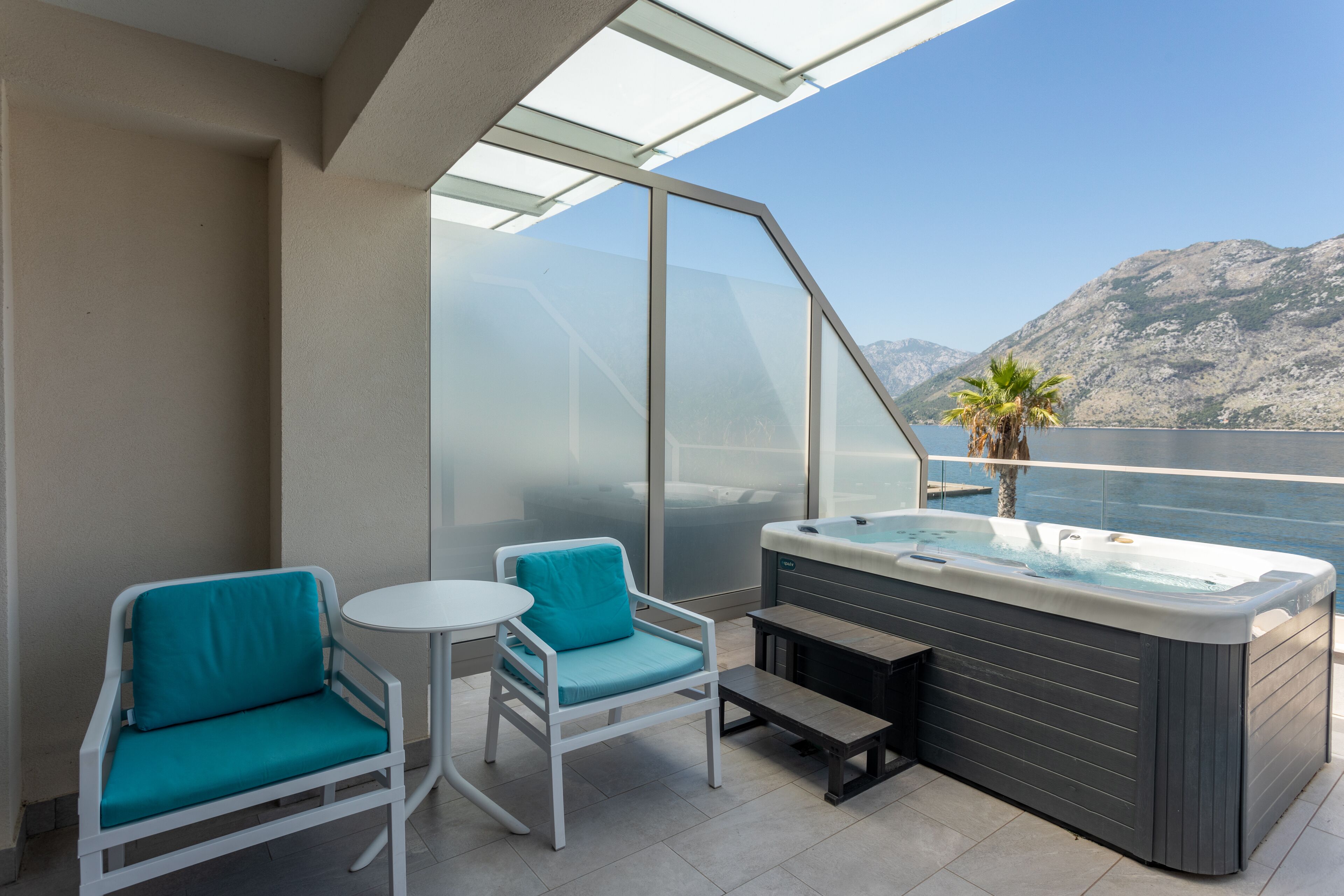 A balcony with two teal chairs, a small table, and a hot tub.