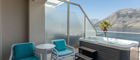 A balcony with two teal chairs, a small table, and a hot tub.