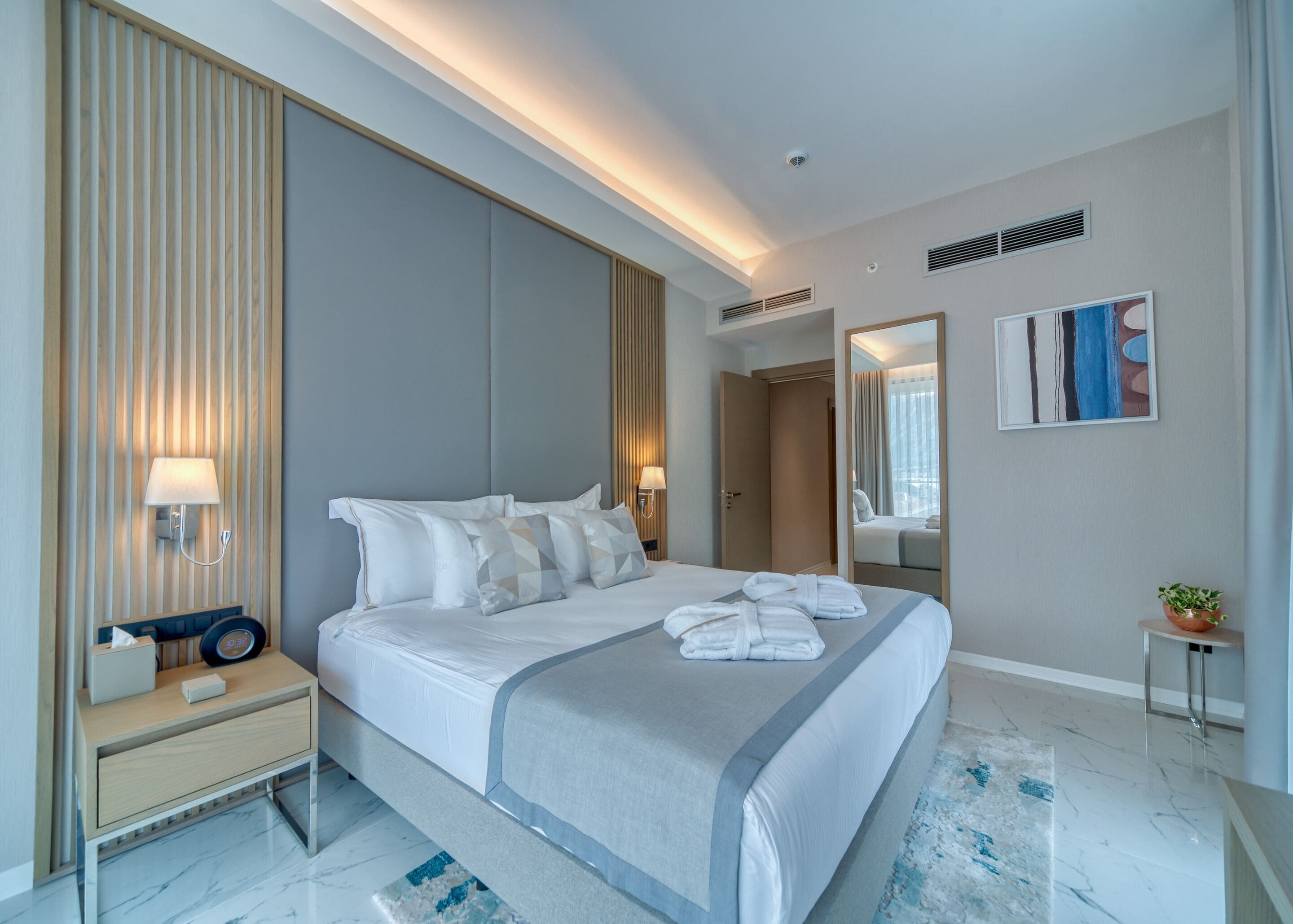 Une chambre d’hôtel moderne avec un grand lit, des lampes de chevet, une table de chevet, un miroir et une plante en pot.