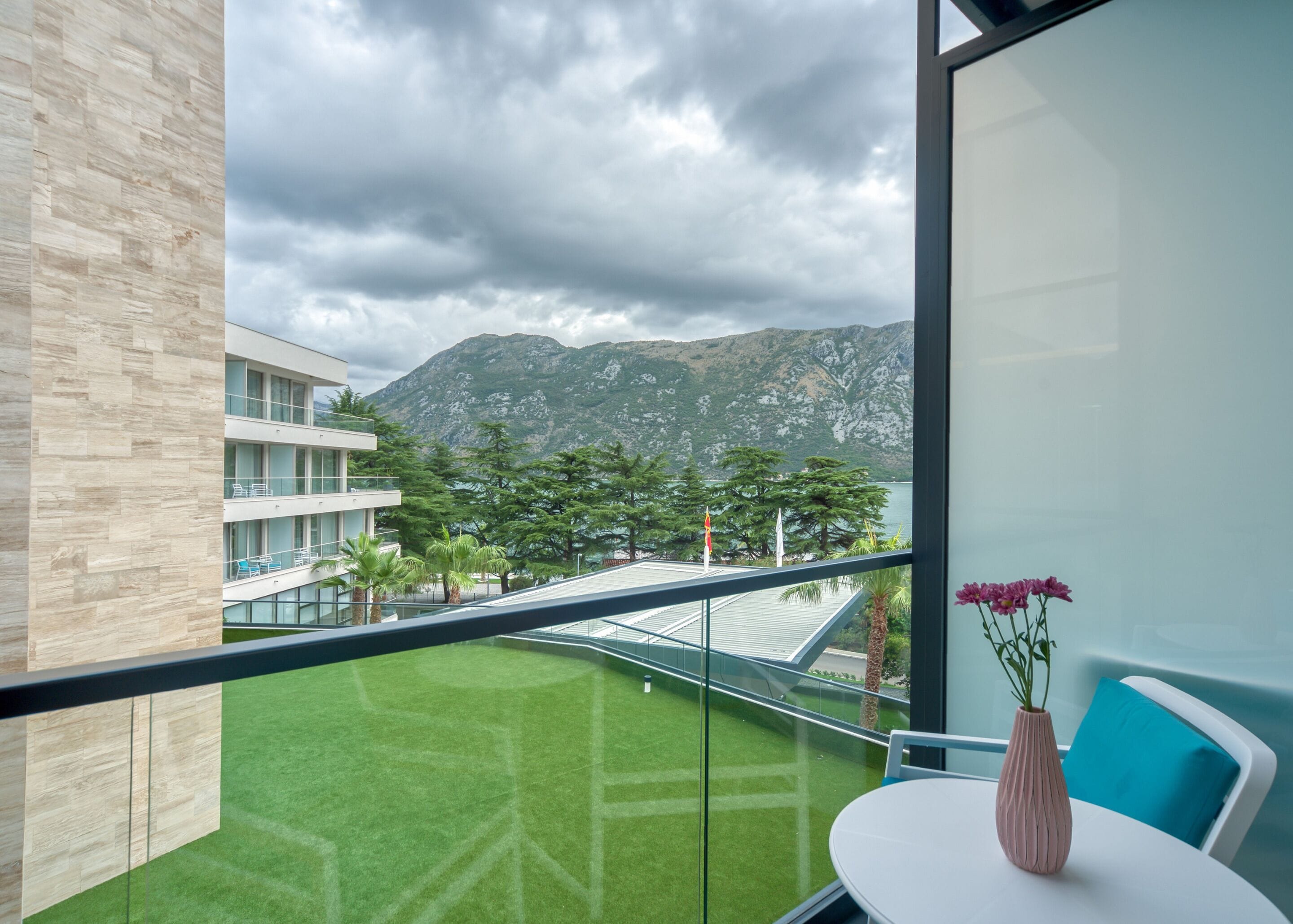 A modern hotel room with a balcony, a view of mountains, and a grassy terrace.