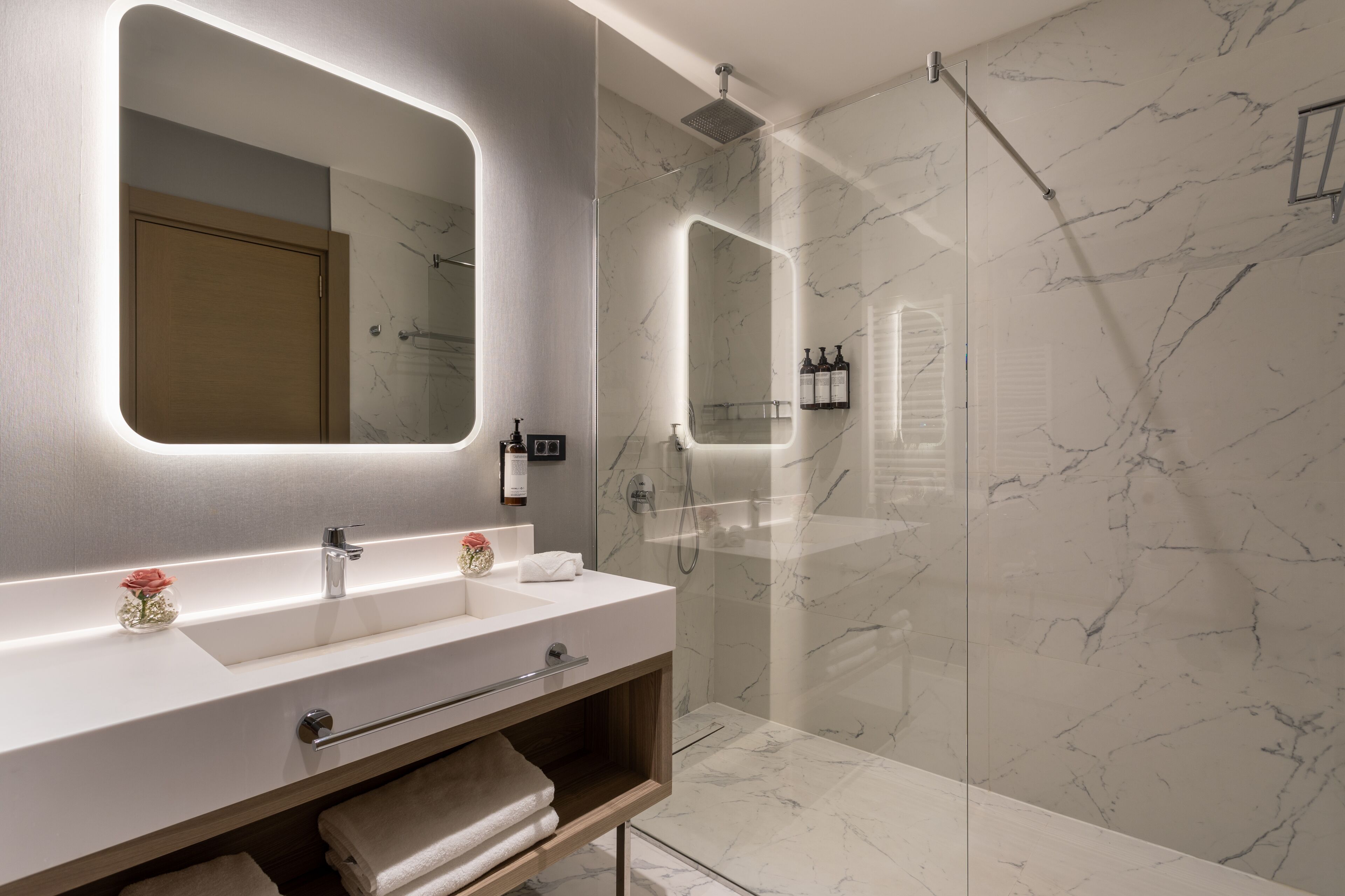 Un baño moderno con un espejo grande, un tocador con lavamanos y una ducha con cerramiento de vidrio.