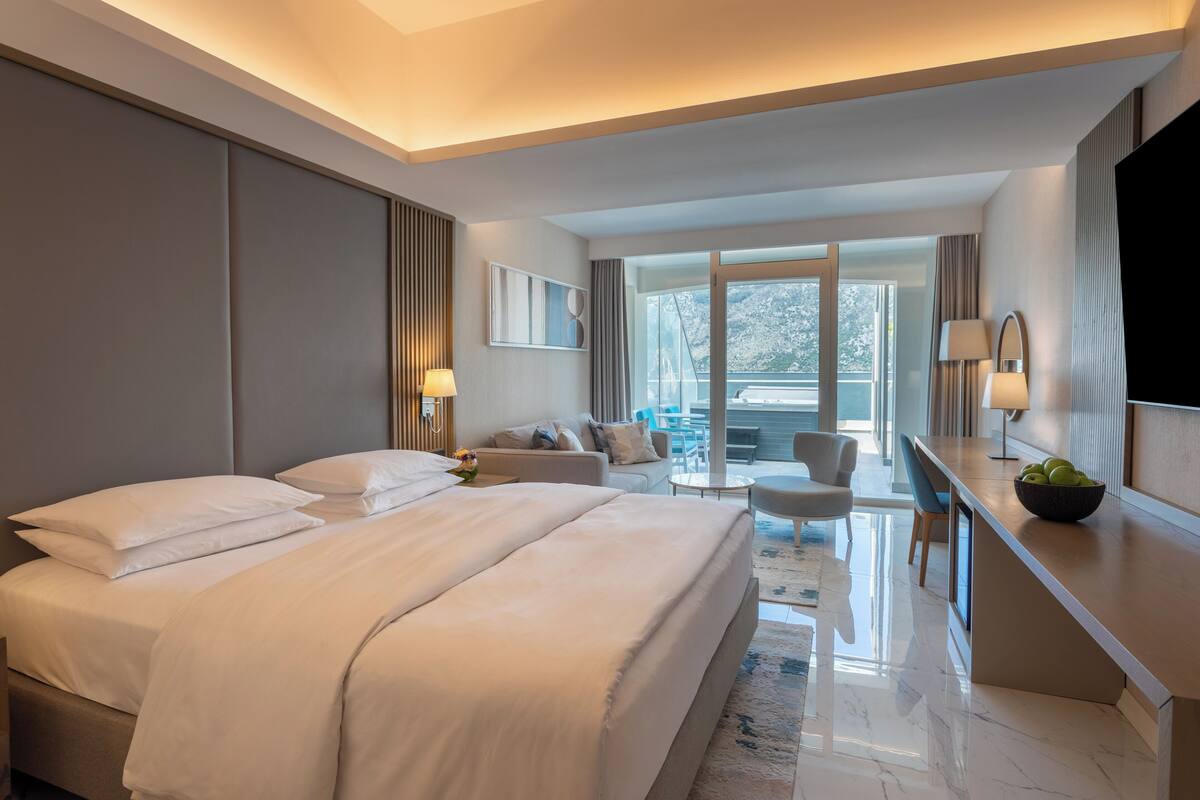 Une chambre d’hôtel moderne dotée d’un grand lit, d’un coin salon avec un canapé et des fauteuils, d’une table à manger et d’un téléviseur.
