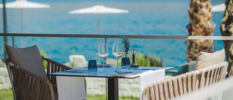 A table set for two with a view of the sea, outdoor chairs, and umbrellas.