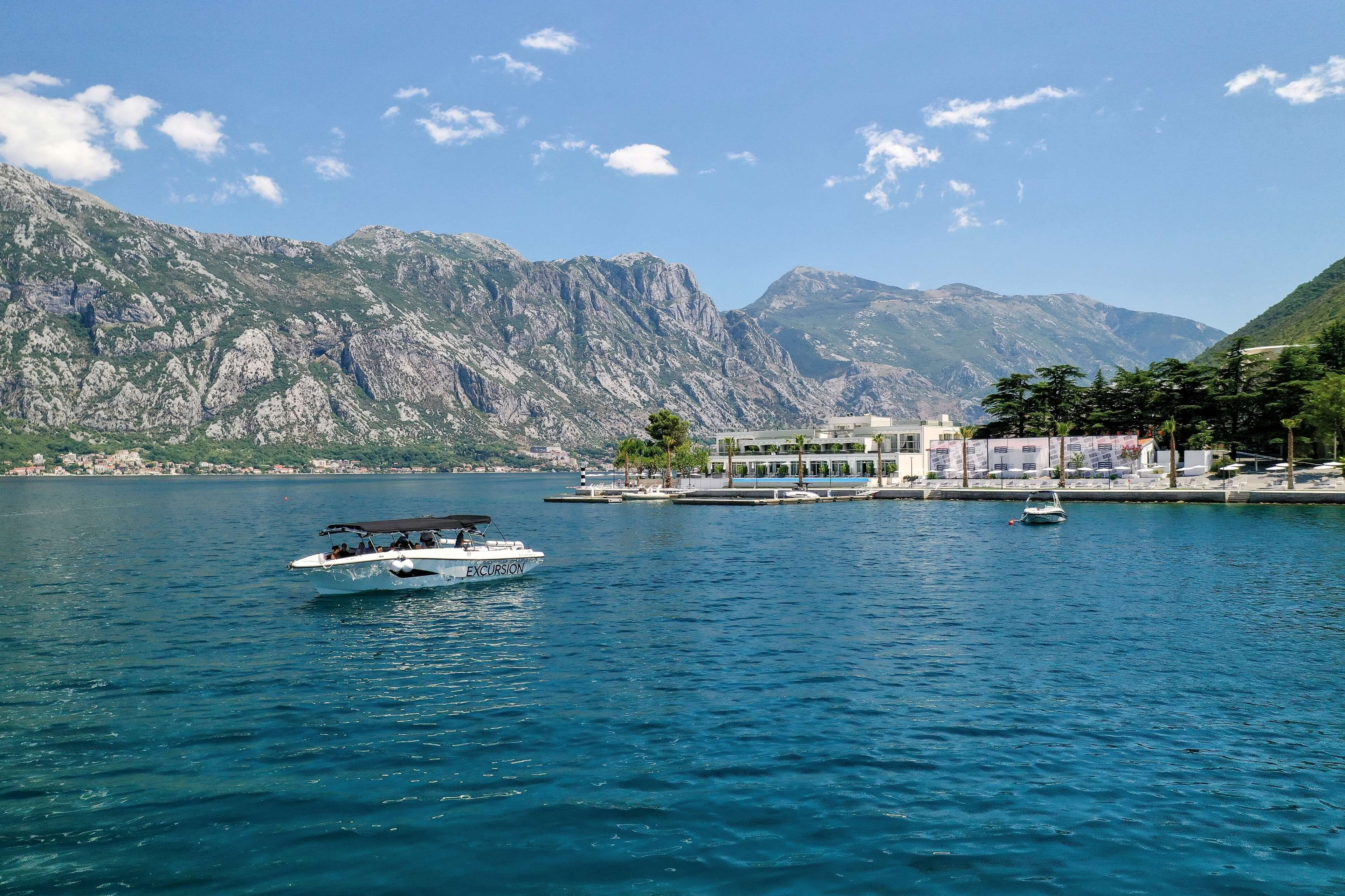 Una barca chiamata "Excursion" su un lago calmo, con montagne sullo sfondo.