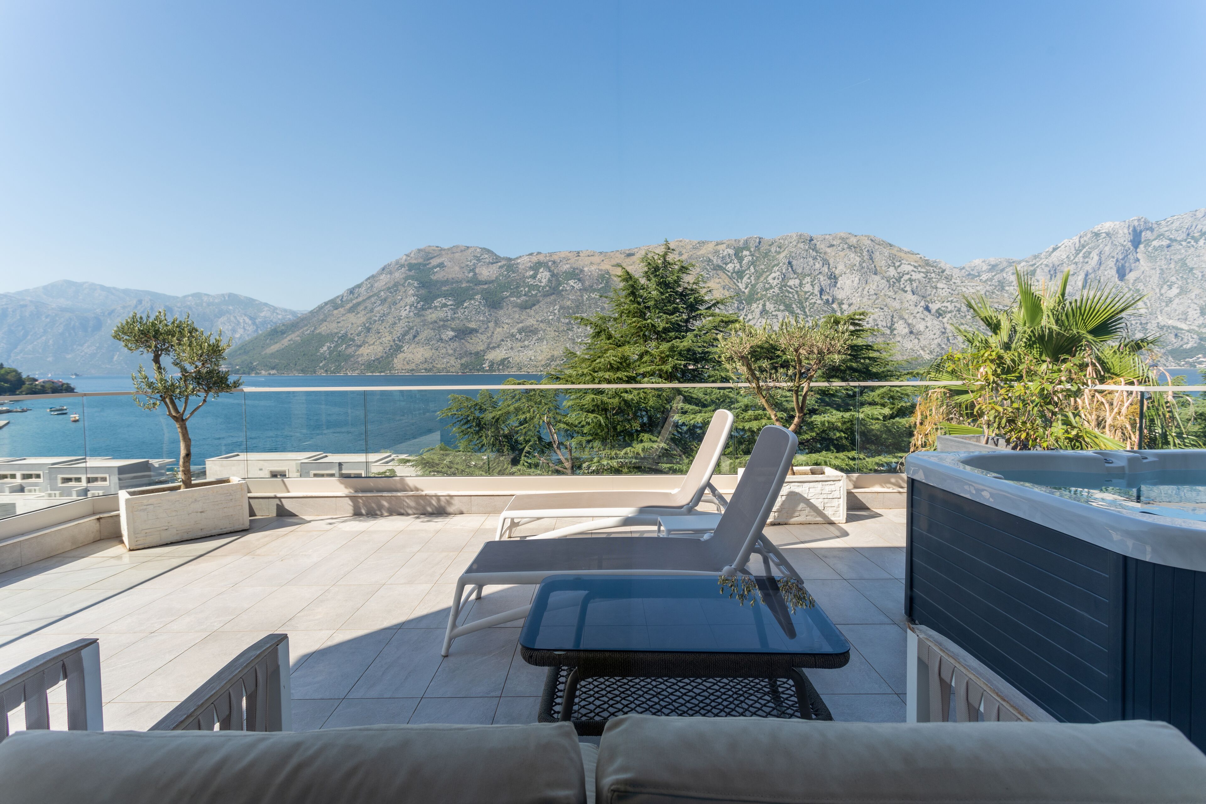 Une terrasse avec deux chaises longues, un jacuzzi et une vue sur la mer et les montagnes.