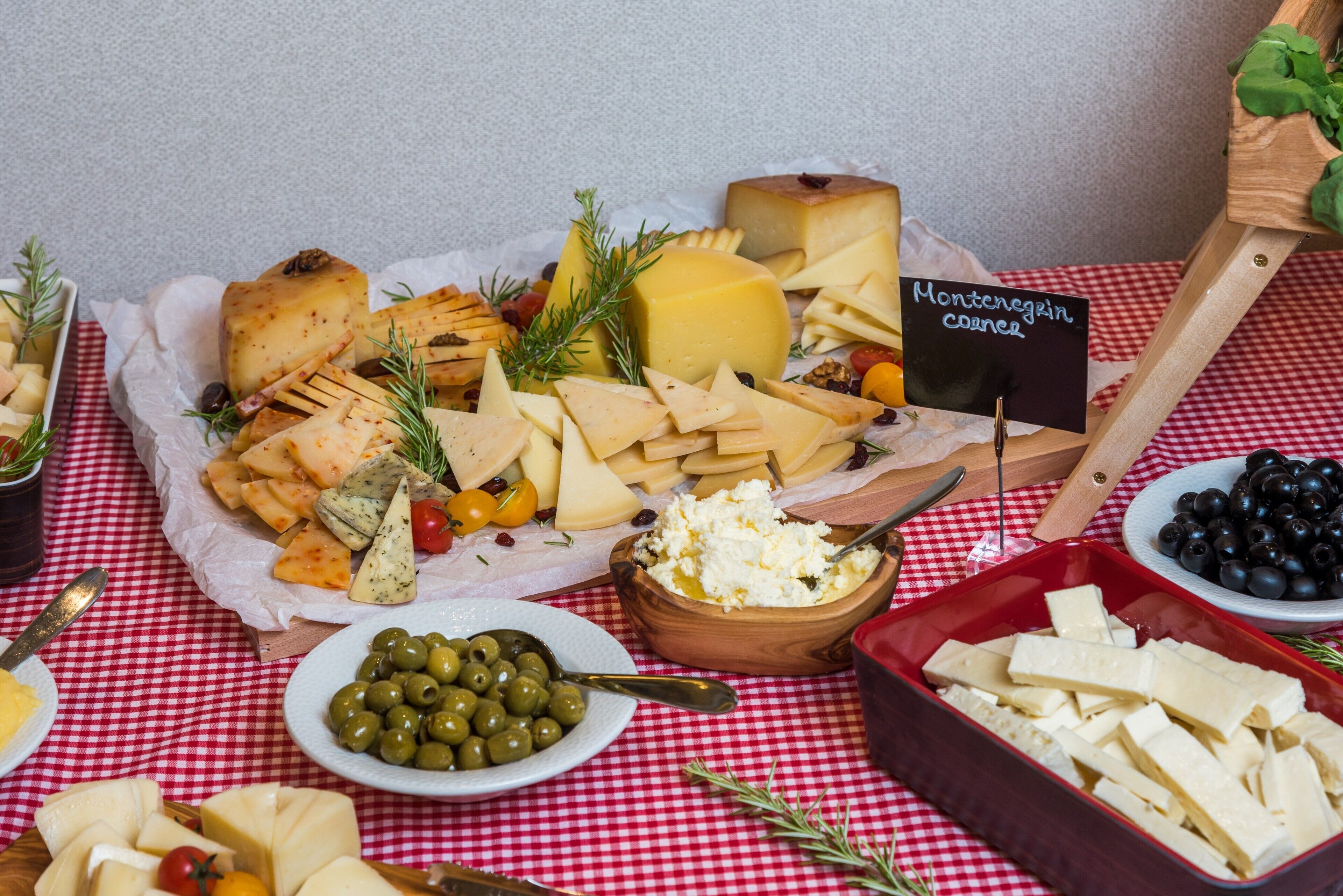 Uma tábua de queijos com diversos tipos de queijo, azeitonas e uma placa indicando 'queijo Montenegro'.