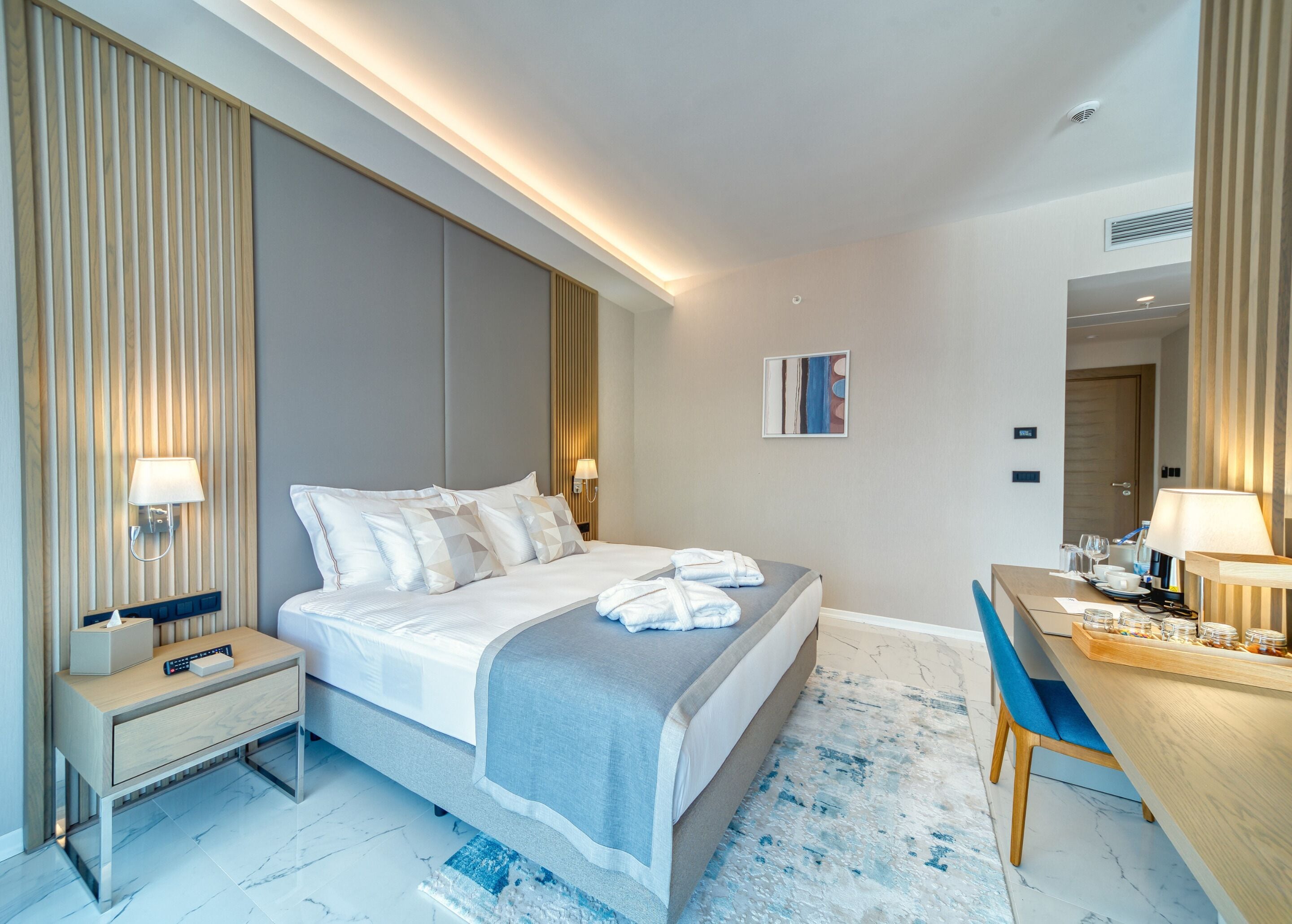 A modern hotel room with a large bed, bedside tables, a desk, and a chair.