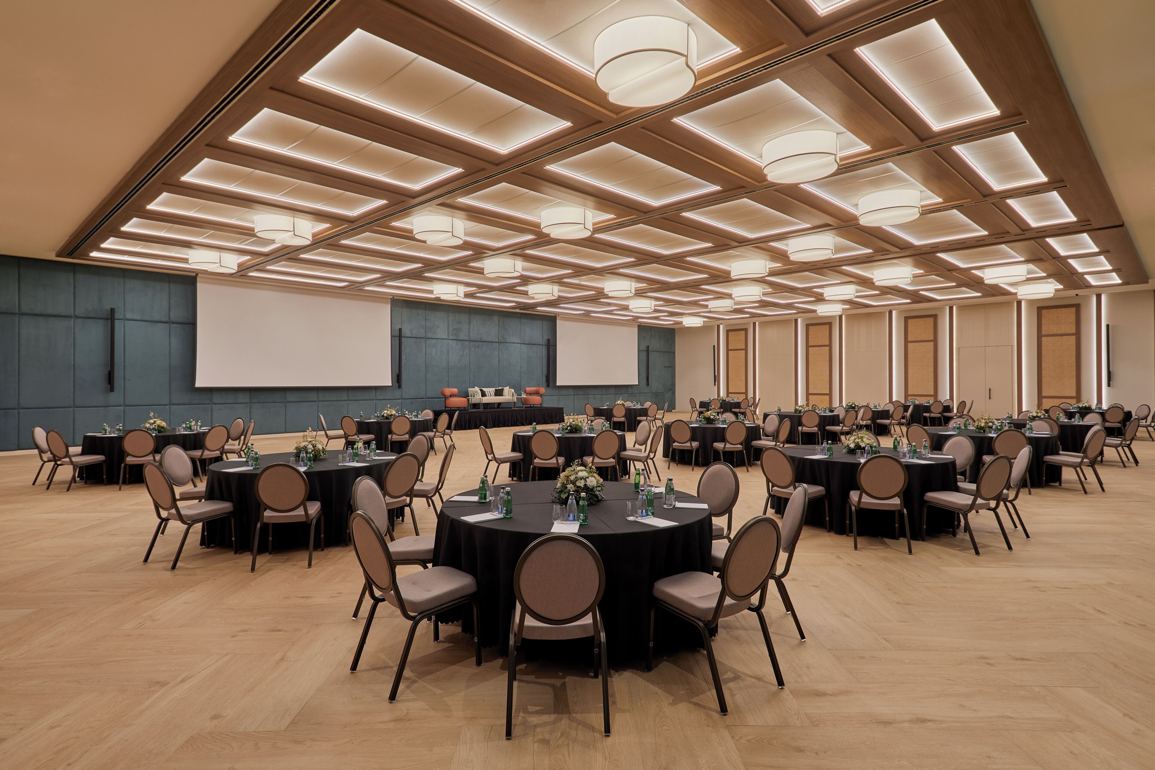 Un salón de conferencias con varias mesas redondas, sillas y una pantalla grande.