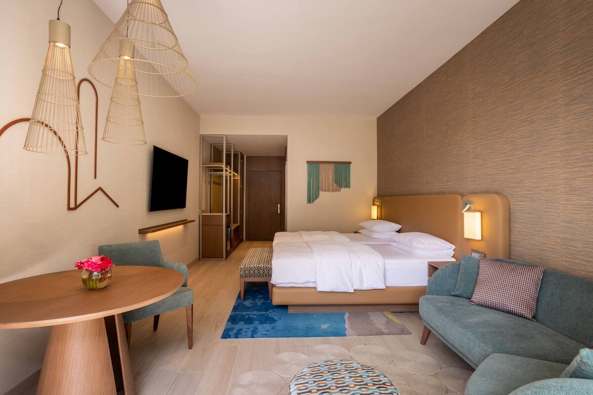 Une chambre d’hôtel avec un lit, un canapé, une table à manger décorée de fleurs et des lampes suspendues.