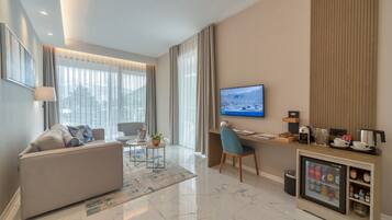 A modern hotel room with a sofa, a desk, a television, and a minibar.