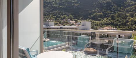 A balcony with a glass railing overlooking a pool and a mountainous landscape.