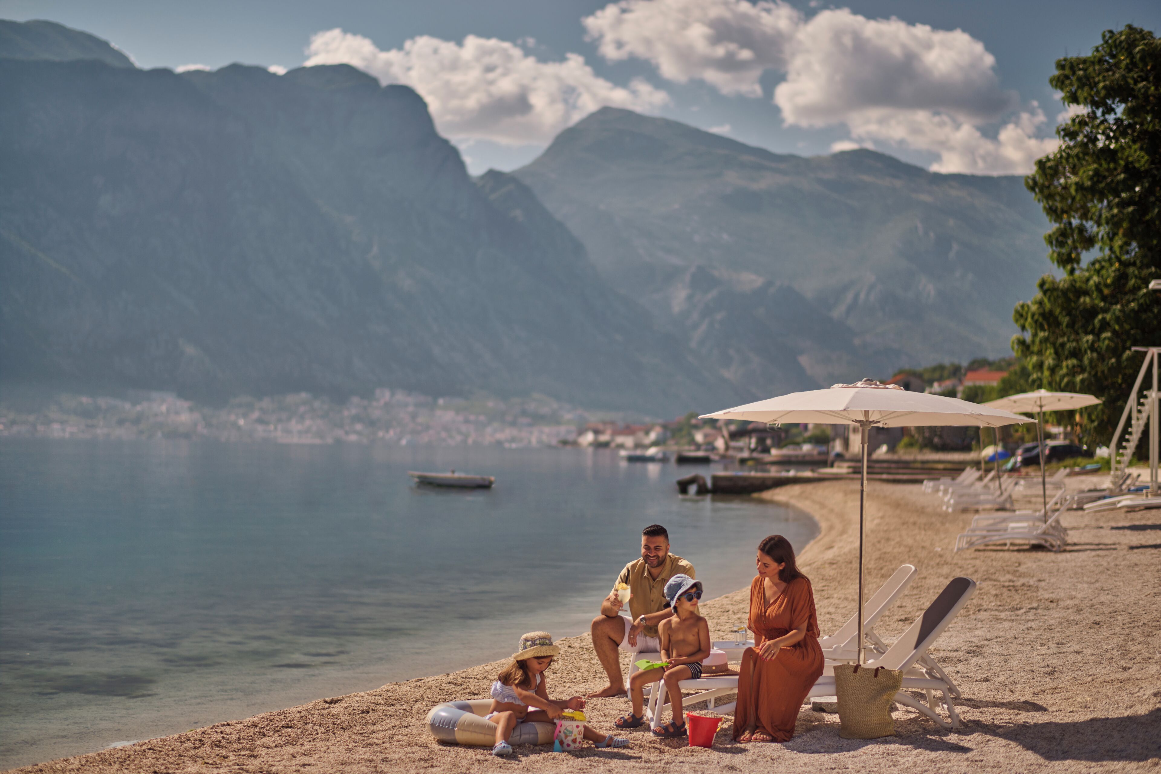 A beach with mountains in the background, a clear sky, and people relaxing on the sand.
