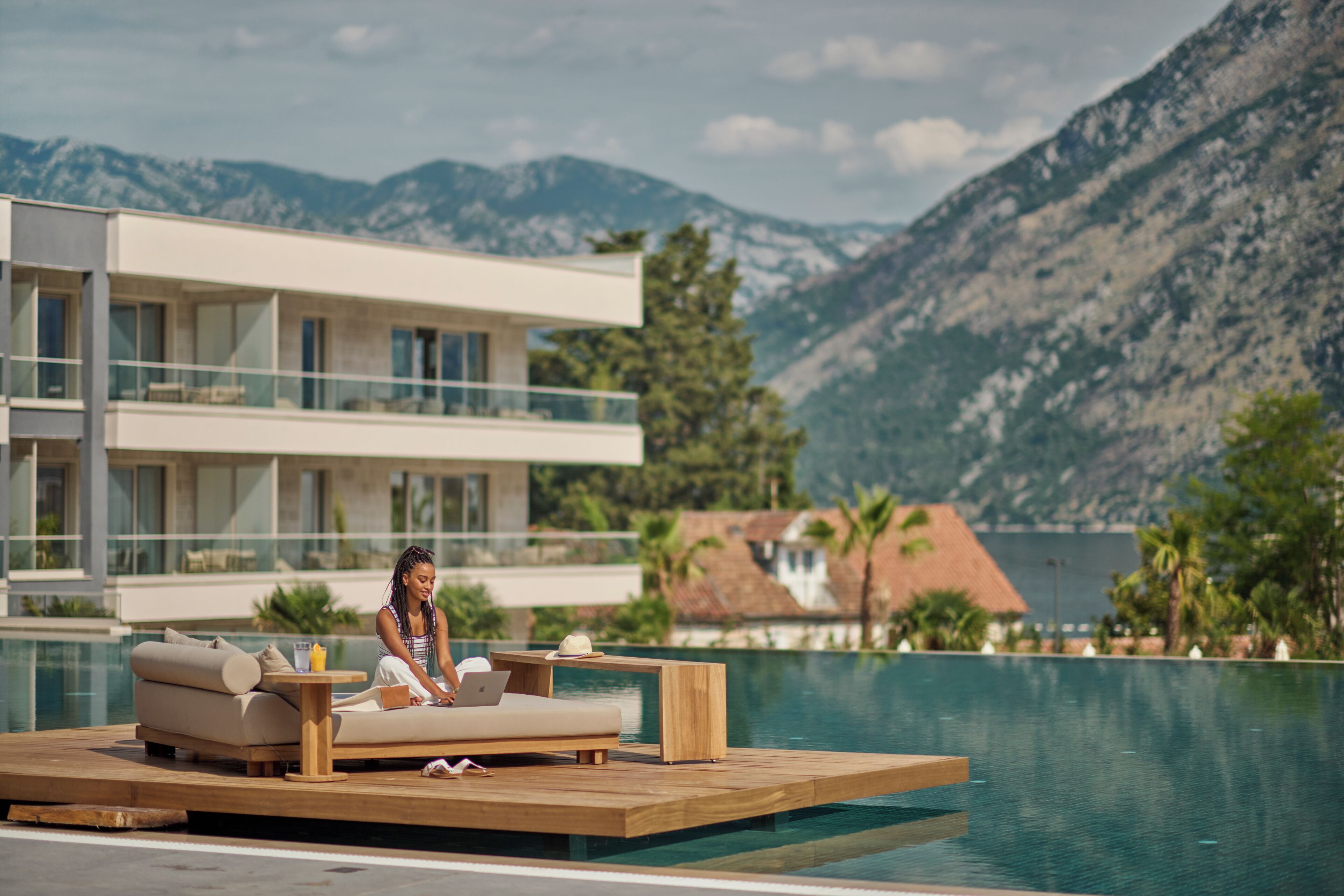 A modern hotel with a pool, a lounge area with a sofa and a table, and a mountain view.