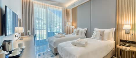 Una habitación de hotel moderna con dos camas, un escritorio con cafetera y un ventanal con cortinas.