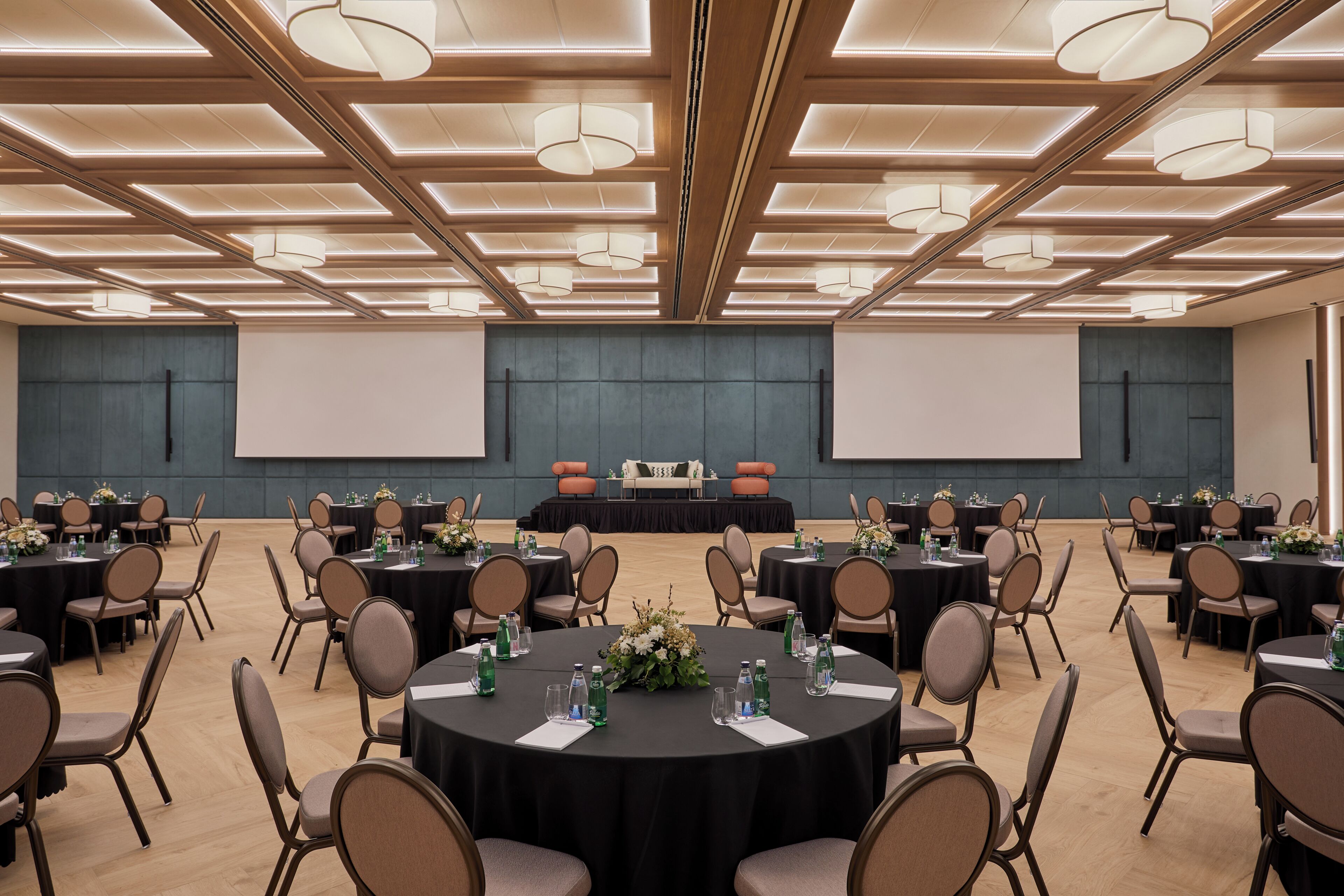 A conference room with multiple tables, chairs, and a stage with a screen.