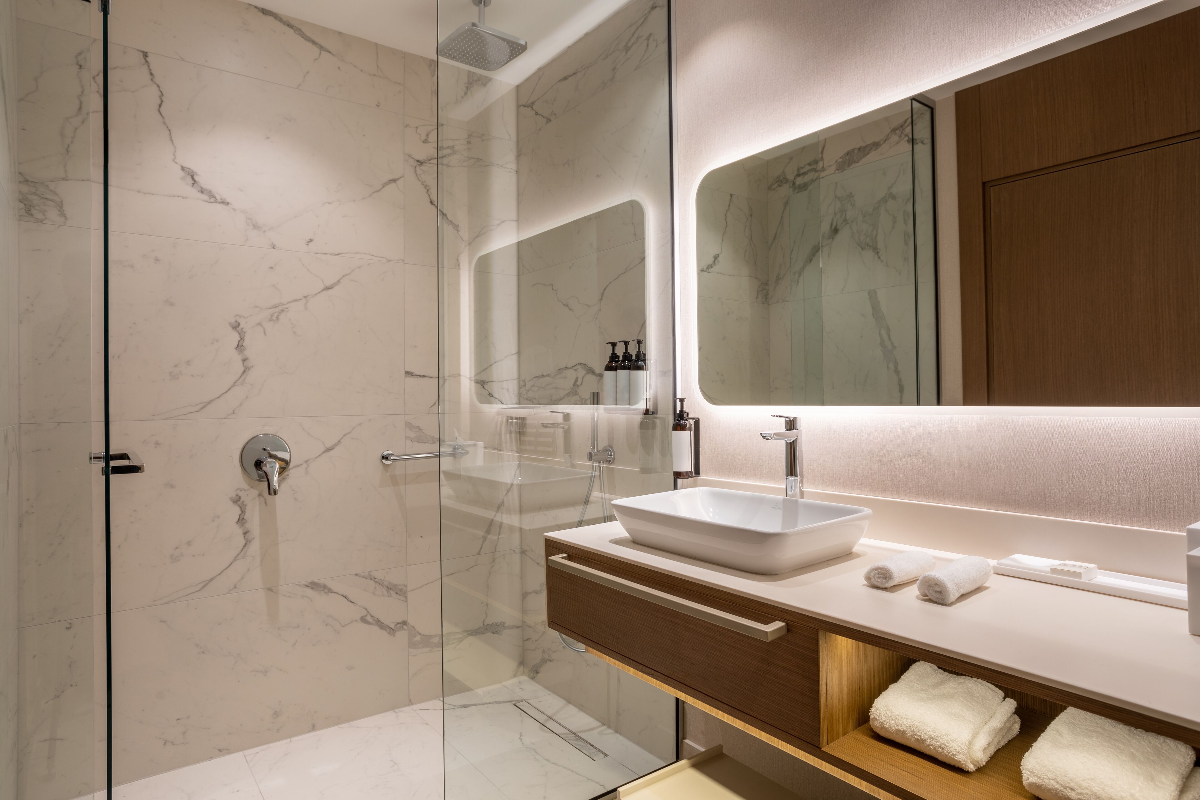 A modern bathroom with a glass-enclosed shower, a white sink, and a wooden vanity.