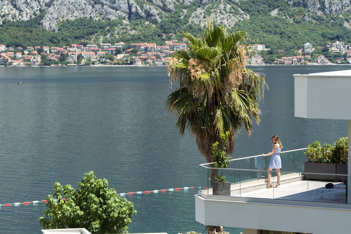 Un balcon avec vue sur un lac, un palmier et un paysage urbain en arrière-plan.