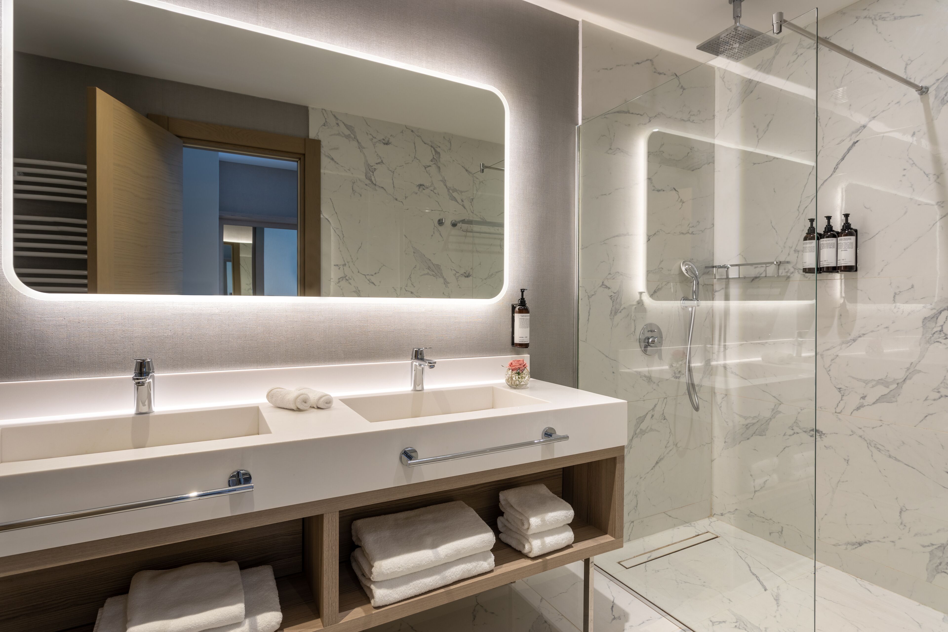 A modern bathroom with a large mirror, two sinks, a glass shower enclosure, and a towel rack.