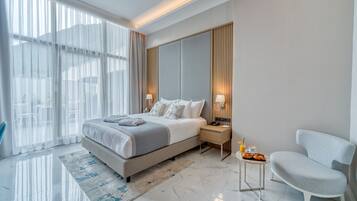 A modern hotel room with a large bed, a bedside table with a lamp, a chair, and a view of the outdoors.