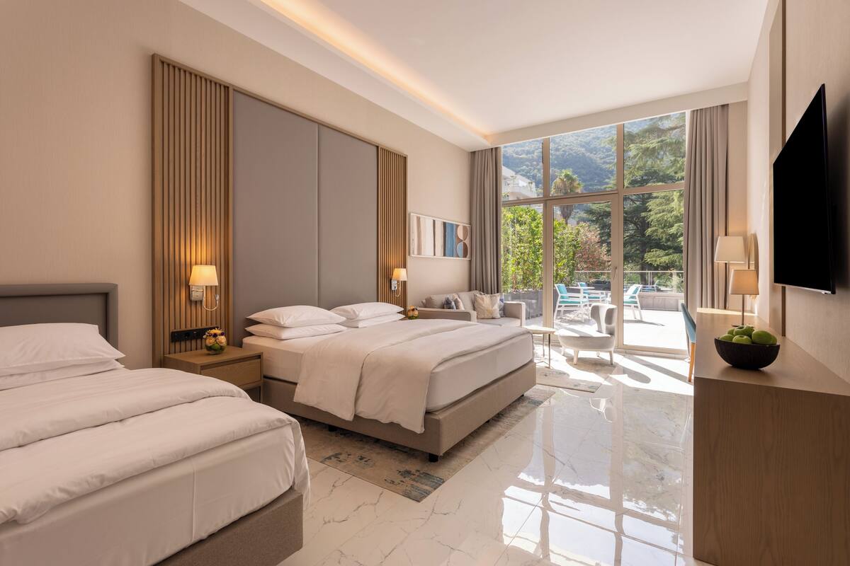 Une chambre d’hôtel moderne dotée d’un grand lit, d’une télévision et d’un balcon offrant une vue sur les montagnes.
