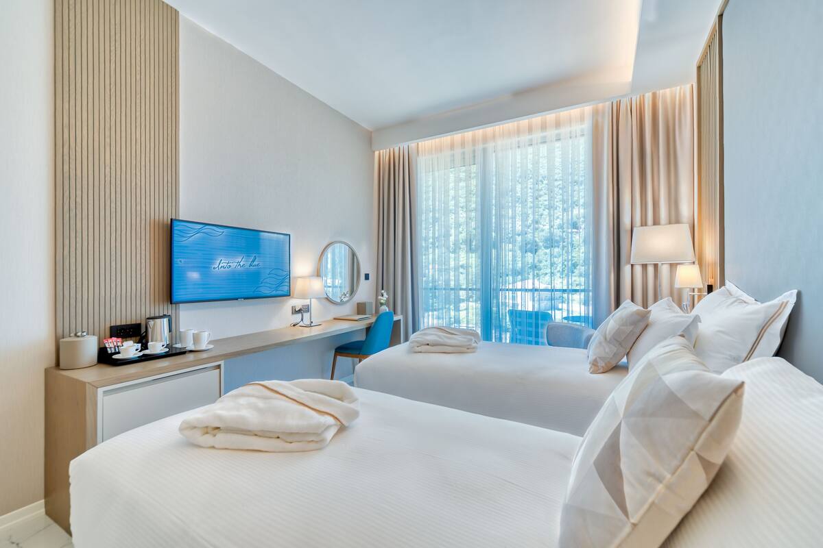 Une chambre d’hôtel avec deux lits, un bureau avec un ordinateur, une télévision et une fenêtre avec des rideaux.
