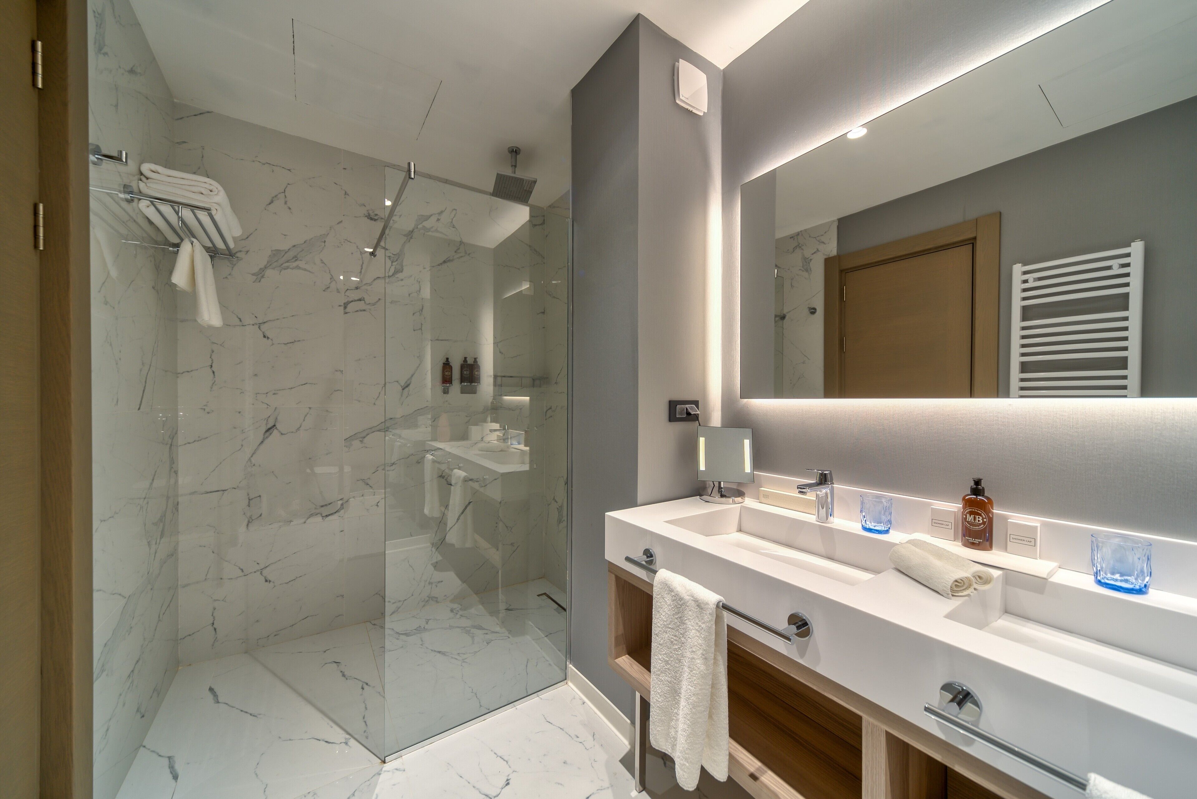 A modern bathroom with a glass-enclosed shower, a large mirror, and a vanity with a sink and towel rack.
